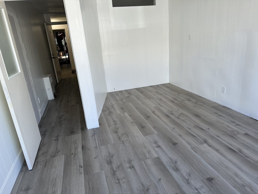 Finished grey vinyl plank floor through a room & hallway